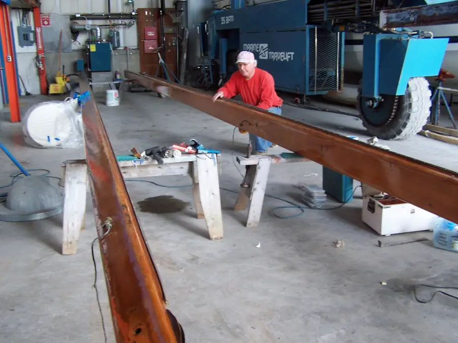 Crew member varnishing a wooden mast in the shop
